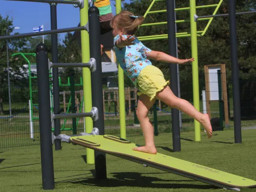 Child balancing on inclined playground ramp, arms outstretched.