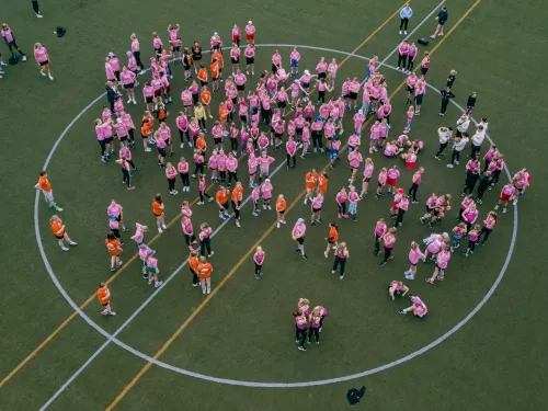 Crowd of people in pink and orange shirts on a sports field.