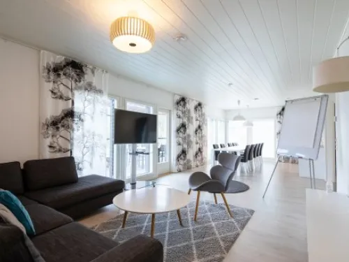 Tilava, vaalea olohuone, jossa sohva, televisio, lepotuolit ja pöytä.