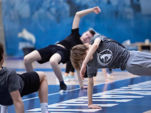 Nuoret harjoittelevat voimistelusalissa sinisellä alustalla.