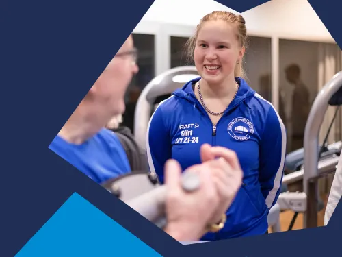 Punahiuksinen nainen sinisessä urheiluvaatteessa hymyilee kuntosalilla.