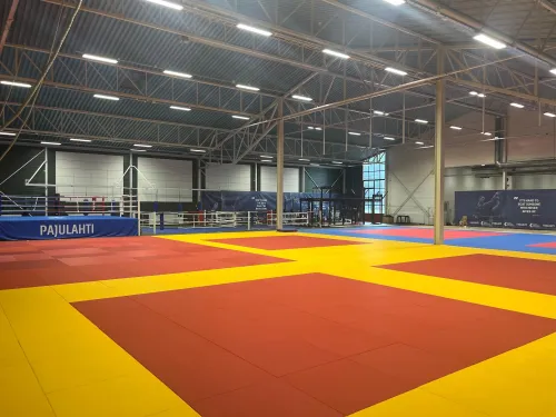 Pajulahden kamppailuareena. Tyhjä judohalli, värikkäät tatamit, teräksiset kattopalkit.