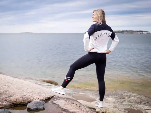 Nainen seisoo rannalla, katsoo merelle pukeutuneena urheiluvaatteisiin.