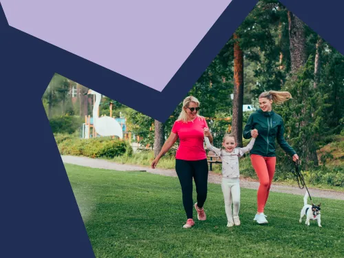 Mummo, lapsi ja äiti kävelevät käsi kädessä Pajulahden rannalla ja pieni koira kulkee heidän vierellään hihnassa.