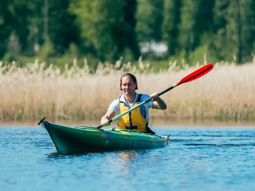 Mies meloo vihreässä kajakissa järvellä, taustalla metsää ja kaislikkoa.
