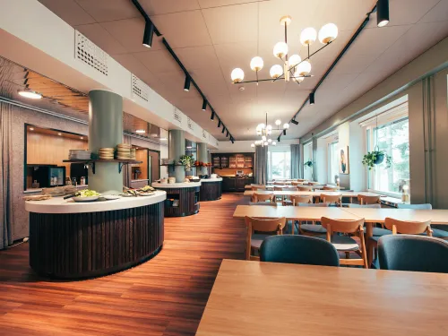 Tilava, valoisa ja moderni ruokailutila puupöydillä ja isoilla ikkunoilla.