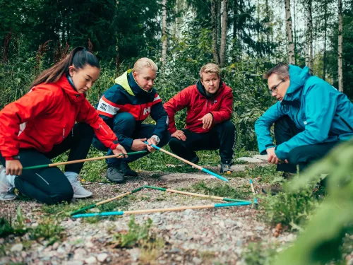 Neljä ihmistä metsässä tutkimassa karttaa kankaalla sauvojen avulla.