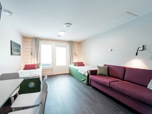 Valoisa hotellihuone, kaksi sänkyä, sohvapöytä, violetti sohva.