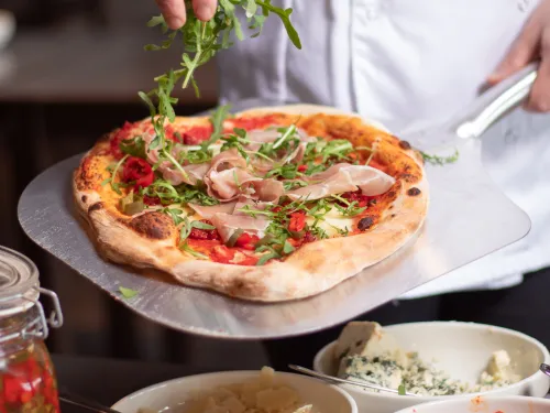 Kokki lisää pizzan päälle rucolaa keittiössä.