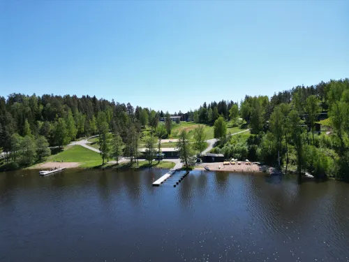 Järvimaisema laiturilla, vihreää metsää taustalla, sininen taivas.