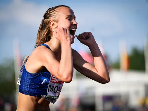 Urheilija juhlii iloisesti kentällä, taustalla näkyy lipputankoja.