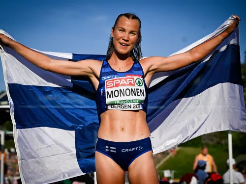 Yleisurheilija hymyilee ja pitää Suomen lippua.