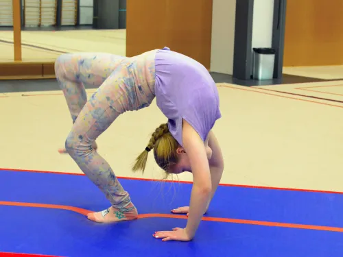 Salilla jumppapatjalla nuori tyttö tekee kaaritaivutuksen.