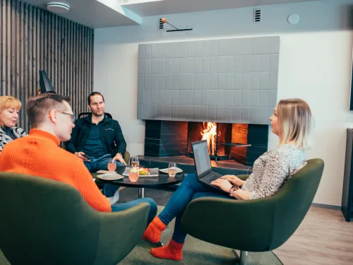 Neljä ihmistä kokoustaa takkatulen äärellä kannetavat tietokoneet sylissä.