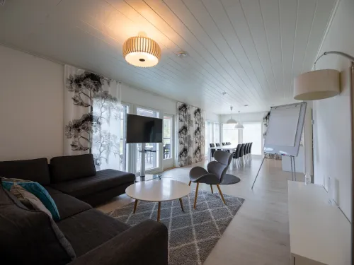 Moderni olohuone, jossa on sohva, televisio, nojatuolit ja ruokapöytä valaistuna.