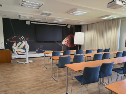 Tyhjä luokkahuone, jossa puiset pöydät ja siniset tuolit.