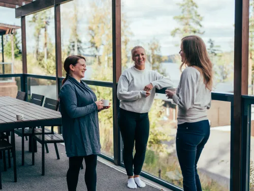 Kolme naista juttelee Villa Kallion terassilla, jossa on järvinäköala.