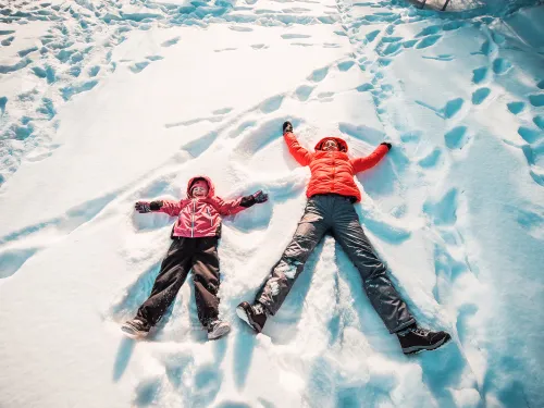 Äiti ja tytär tekevät lumessa lumienkeleitä.