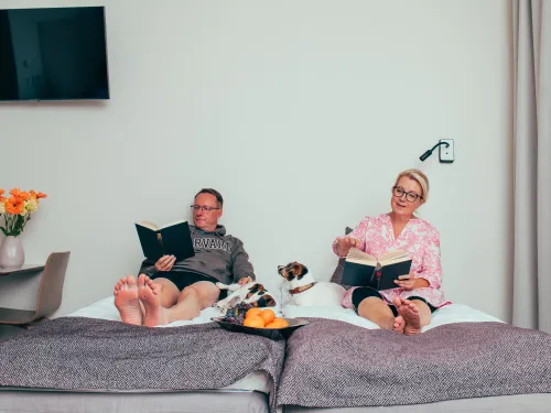 Pariskunta lukee sängyssä kirjojaan Pajulahden hotellissa koiran makoillessa heidän keskellään.