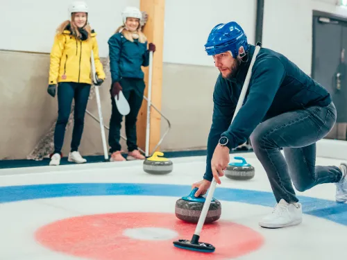 Kisakallion jäähallissa mies on jäällä työntämässä curling-kiveä.
