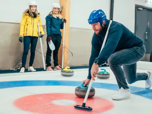 Kisakallion jäähallissa mies on jäällä työntämässä curling-kiveä.