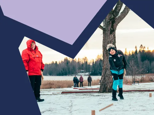 Kaksi iloista naista pelaa mölkkyä lumisella maalla.