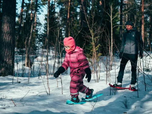 Tyttö ja nainen lumikenkäilevät lumisessa metsässä.