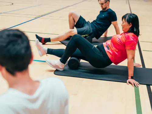 Kaksi ihmistä pyörittelee foam rollereita jalkansa alla.