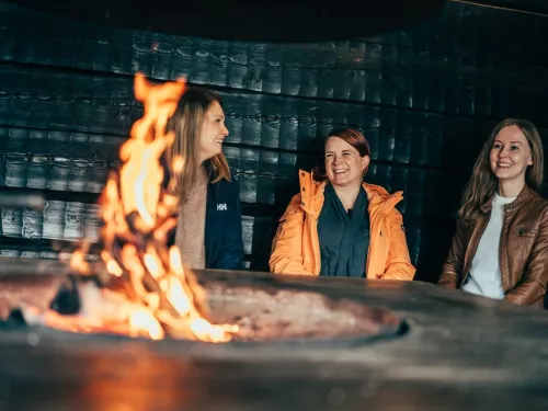 Kolme nauravaa naista istuu nuotion äärellä.