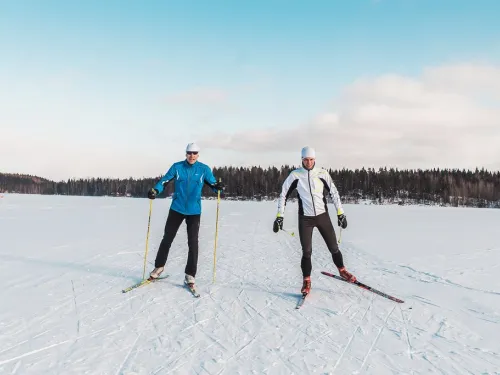 Kaksi ihmistä hiihtää lumisella järvellä aurinkoisena päivänä.