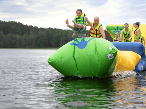 Lapsi hyppää ilmapatjalta järveen muiden katsoessa taustalla.