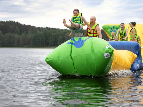 Lapsi hyppää ilmapatjalta järveen muiden katsoessa taustalla.