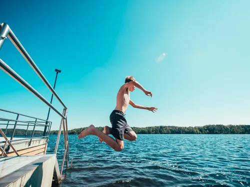 Mies hyppää laiturilta veteen kirkkaana, aurinkoisena päivänä.