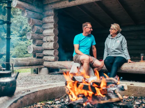 Couple sitting by a campfire in a log cabin, smiling at each other.