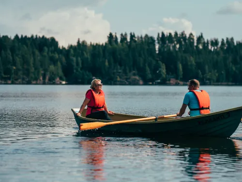 Two people in life vests rowing a boat on a calm lake.