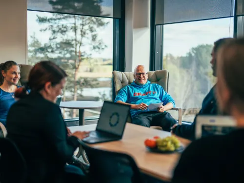 Ihmiset työskentelevät Omenatarhan kokoustilassa läppäreillä ja ikkunoista avautuu järvi- ja metsänäkymä.