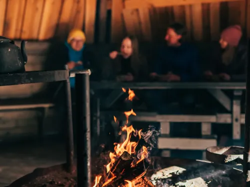 Suurkodassa on nuotio ja taustalla ihmisiä syömässä.