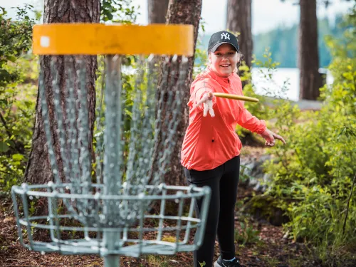 Hymyilevä tyttö heittää kiekkoa frisbeegolf-koriin