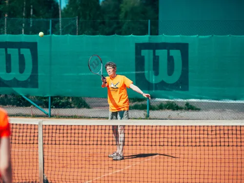 Tennis player in orange shirt serving on clay court.
