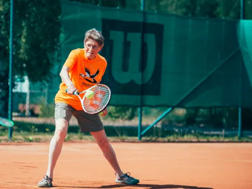 Tennis player in orange shirt on clay court, mid-swing.