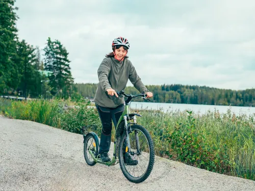 Nainen potkii kickbikella järven rannalla.