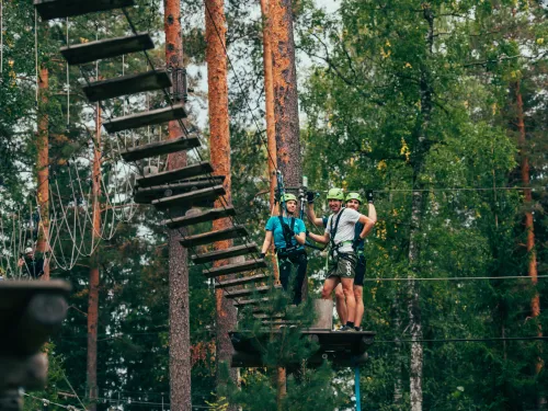 Kolme henkilöä seikkailupuistossa puusillalla metsässä.