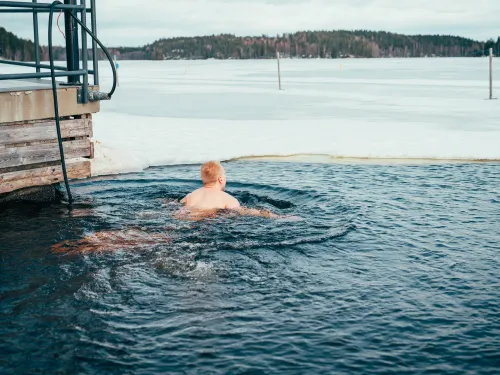 Person swimming in icy lake near a wooden platform.