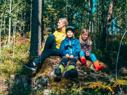 Perhe istuu kivellä syksyisessä metsässä