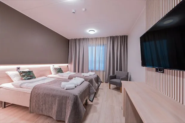 Kaksi sänkyä hotellihuoneessa, iso televisio seinällä.