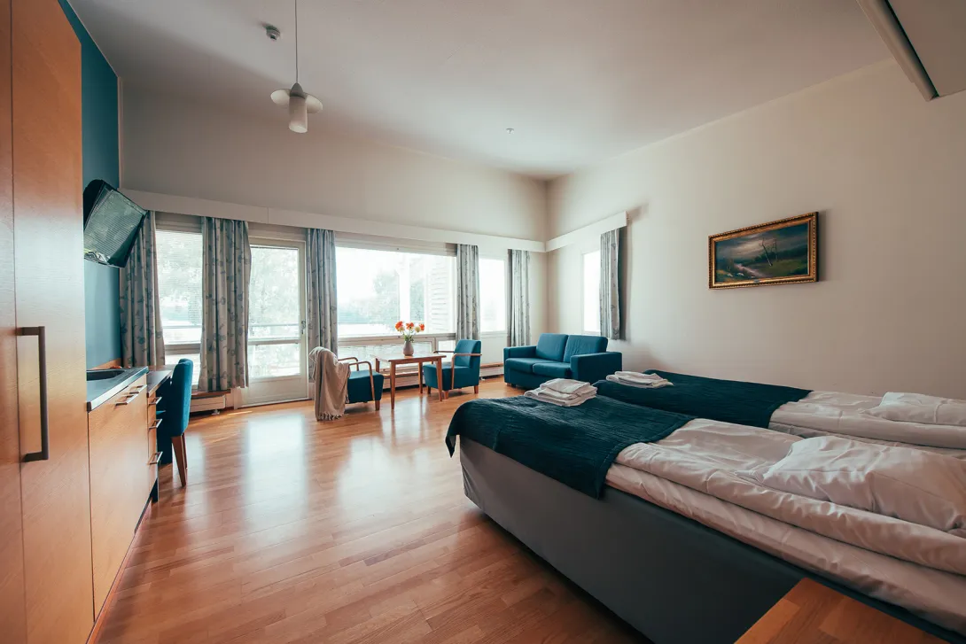 Tilava hotellihuone, kaksi sänkyä, sohva ja suuri ikkuna.