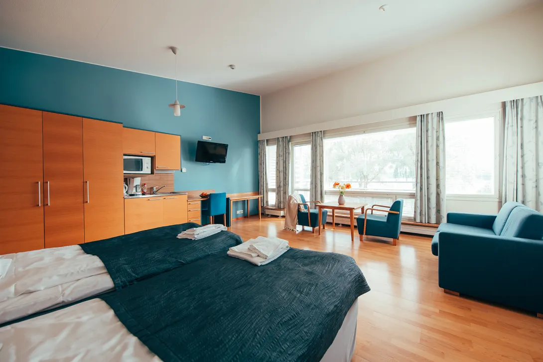 Hotellihuone, iso ikkuna, siniset ja puiset sävyt, leveä sänky ja työpöytä.