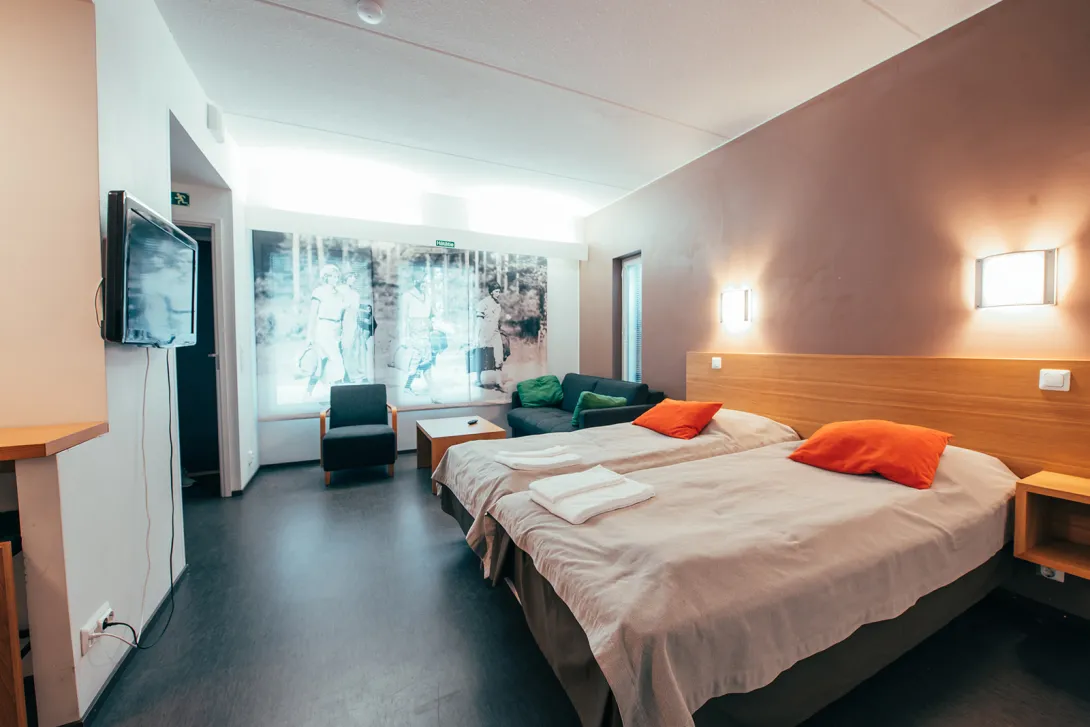 Moderni hotellihuone kahdella sängyllä, seinällä taulu ja TV.