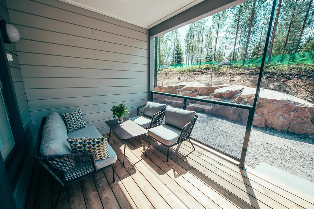 Veranta, jossa sohva, kaksi tuolia ja pöytä; taustalla metsä.