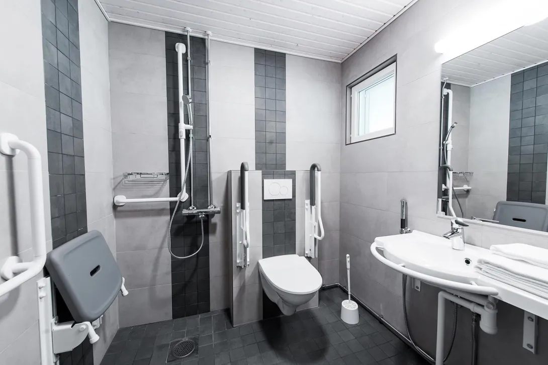 Esteetön kylpyhuone, jossa on suihku ja wc-tukikaiteineen.